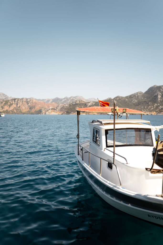 White fishing boat on calm Mediterranean sea with mountains under clear blue sky.